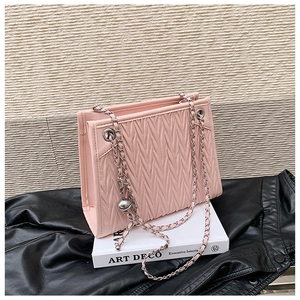 Detail of pink quilted shoulder bag with woven silver chain strap on a book