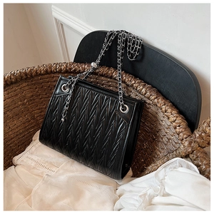 Detail of black quilted tote bag with metallic chain strap on a woven chair background