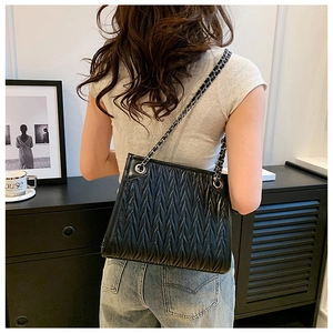 Detail view of black quilted V-pattern leather surface with silver chain strap
