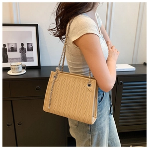 Detail of beige quilted shoulder bag with chic silver chain strap on a female model