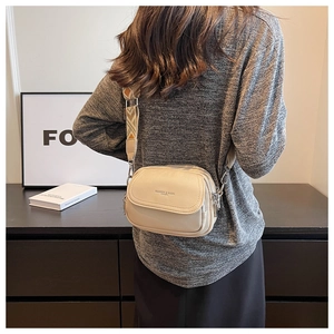 Détail du sac bandoulière en cuir crème avec lettrage doré et sangle tissée à motifs