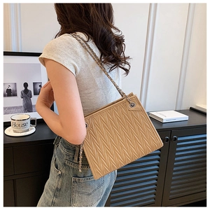 Quilted beige shoulder bag with V-shaped stitching and woven chain strap on a model