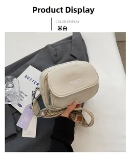 Détail d'un sac bandoulière en cuir crème avec large sangle à motifs sur un blazer