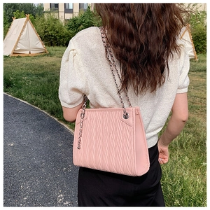 Pink quilted shoulder bag with silver chain strap shown in an outdoor lifestyle setting