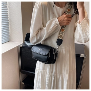 Détail d'un sac bandoulière noir avec une large sangle en tissu jacquard ethnique