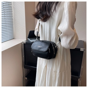 Détail du sac bandoulière noir en cuir grainé avec trois zips et bandoulière tissée