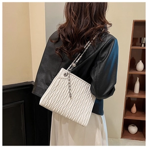 Detail view of white pleated leather bag with silver chain strap worn by a model