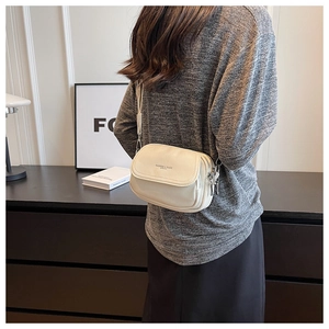 Détail du sac bandoulière blanc crème avec texture litchi et lettrage de mode