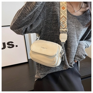 Détail du sac bandoulière blanc cassé avec une sangle large à motifs et cuir grainé