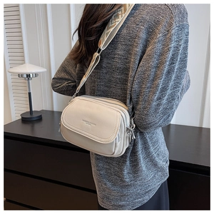 Détail d'un sac bandoulière beige avec trois fermetures éclair et large sangle jacquard