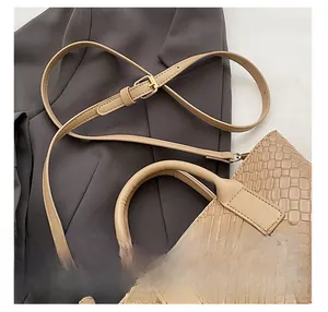 Detail of adjustable slim shoulder strap on beige woven tote bag with gold hardware