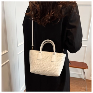 Detail of white woven texture tote bag with leather strap on black suit model outfit