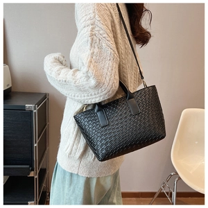 Detail of black woven texture tote bag worn by model over a cream knit sweater