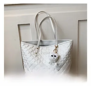 Détail d'un sac cabas blanc matelassé avec des rivets métalliques et un charm en peluche