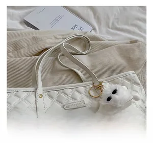 Détail du sac cabas matelassé blanc cassé avec plaque en métal et breloque monstre en peluche