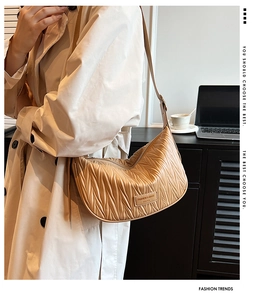 Detail of light brown pleated crescent bag with metal logo and slim leather strap