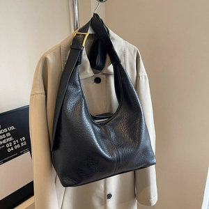 Classic black leather hobo bag with adjustable strap and golden hardware on beige coat