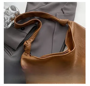 Detailed close-up of a brown leather bucket bag featuring a unique knotted shoulder strap