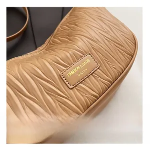 Detail of artistic pleated texture and gold embossed logo on brown shoulder bag