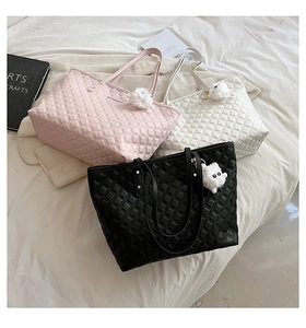 Détail de sacs cabas matelassés rose, blanc et noir avec breloques d'ours sur literie blanche