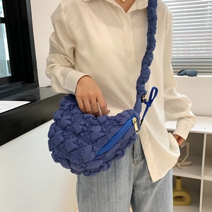 Sac croissant bleu à texture matelassée avec bandoulière porté par un mannequin en studio