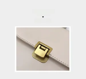 Gros plan sur la boucle dorée rectangulaire d'un sac à bandoulière en cuir beige