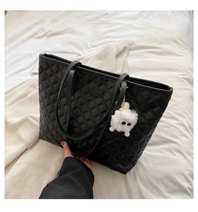 Gros plan d'un sac cabas noir matelassé avec finition en cuir et breloque en peluche