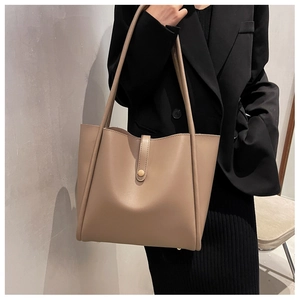 Detail view of khaki tote bag with metal buckle on a model wearing a black blazer