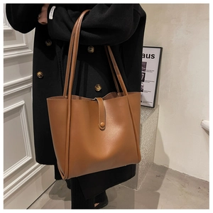 Detailed close-up of brown leather tote bag with thin shoulder straps and buckle detail