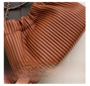 Close-up of brown pleated leather texture and woven metal chain strap on bucket bag