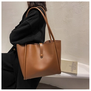 Brown leather tote bag featuring long shoulder straps worn over a black winter coat