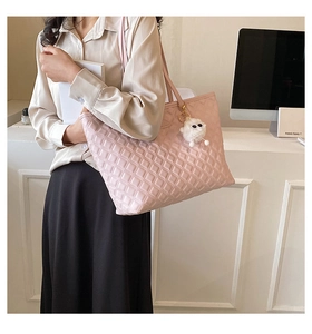 Sac fourre-tout matelassé rose avec pendentif peluche exposé dans un bureau moderne