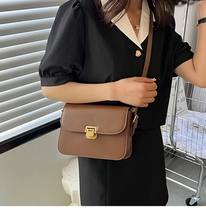 Détail d'un sac à bandoulière en cuir marron avec fermoir métallique doré porté par un modèle