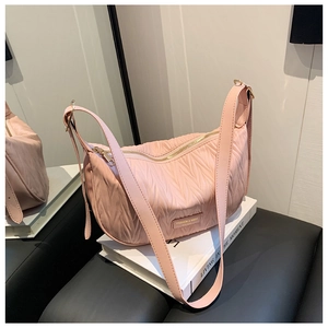 Detail of pink pleated texture shoulder bag with gold metal logo plate on white books
