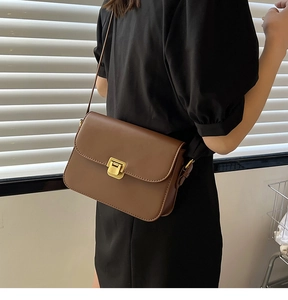 Sac bandoulière en cuir marron avec boucle dorée, porté sur le côté par un mannequin