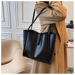 Lifestyle view of a minimalist black leather tote bag worn on shoulder for daily commute