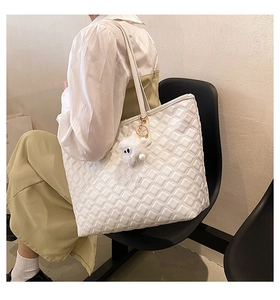 Gros plan sur un sac cabas blanc matelassé avec pendentif en peluche porté par un mannequin