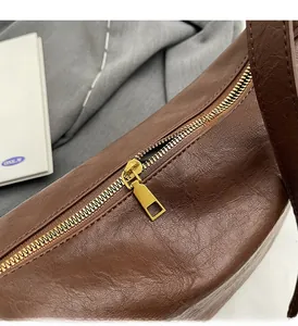Detail view of the retro gold metal zipper on a dark brown leather dumpling shoulder bag
