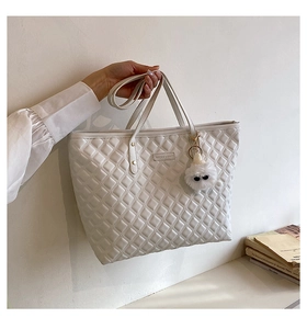 Détail du sac cabas matelassé avec plaque logo en métal et breloque en peluche douce