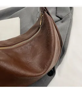 Detail of a brown textured crescent bag featuring a metallic gold zipper and retro style