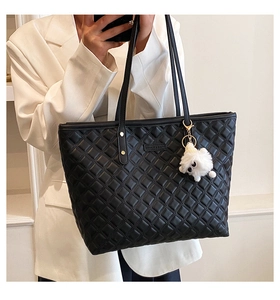 Détail d'un sac cabas noir matelassé avec logo en métal et breloque peluche chien blanc
