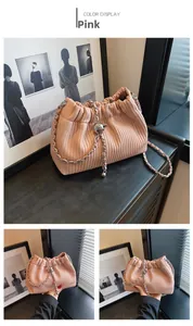 Pink pleated bucket bag with silver chain strap and metal ball charm on wood surface