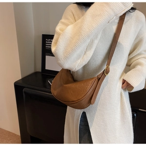 Close-up of brown textured leather hobo bag with adjustable strap on a white sweater