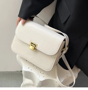 Détail du sac à main en cuir beige minimaliste avec fermoir doré sur un support texturé