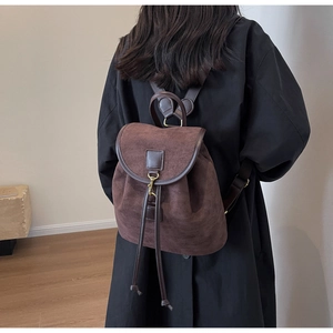 Detail of dark brown matte suede backpack with drawstring closure worn by a model