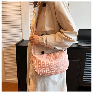 Detail of light pink pleated half-moon shoulder bag worn with a stylish trench coat