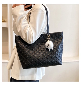 Détail du grand sac cabas noir matelassé avec peluche sur un blazer blanc chic