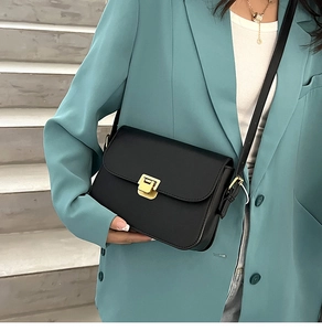 Détail d'un sac à bandoulière noir avec boucle dorée porté par un mannequin chic