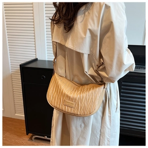 Detail of beige pleated croissant bag with shoulder strap and brand patch on model