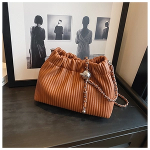 Detail of caramel pleated bucket bag with silver metal ball and chain strap on wood